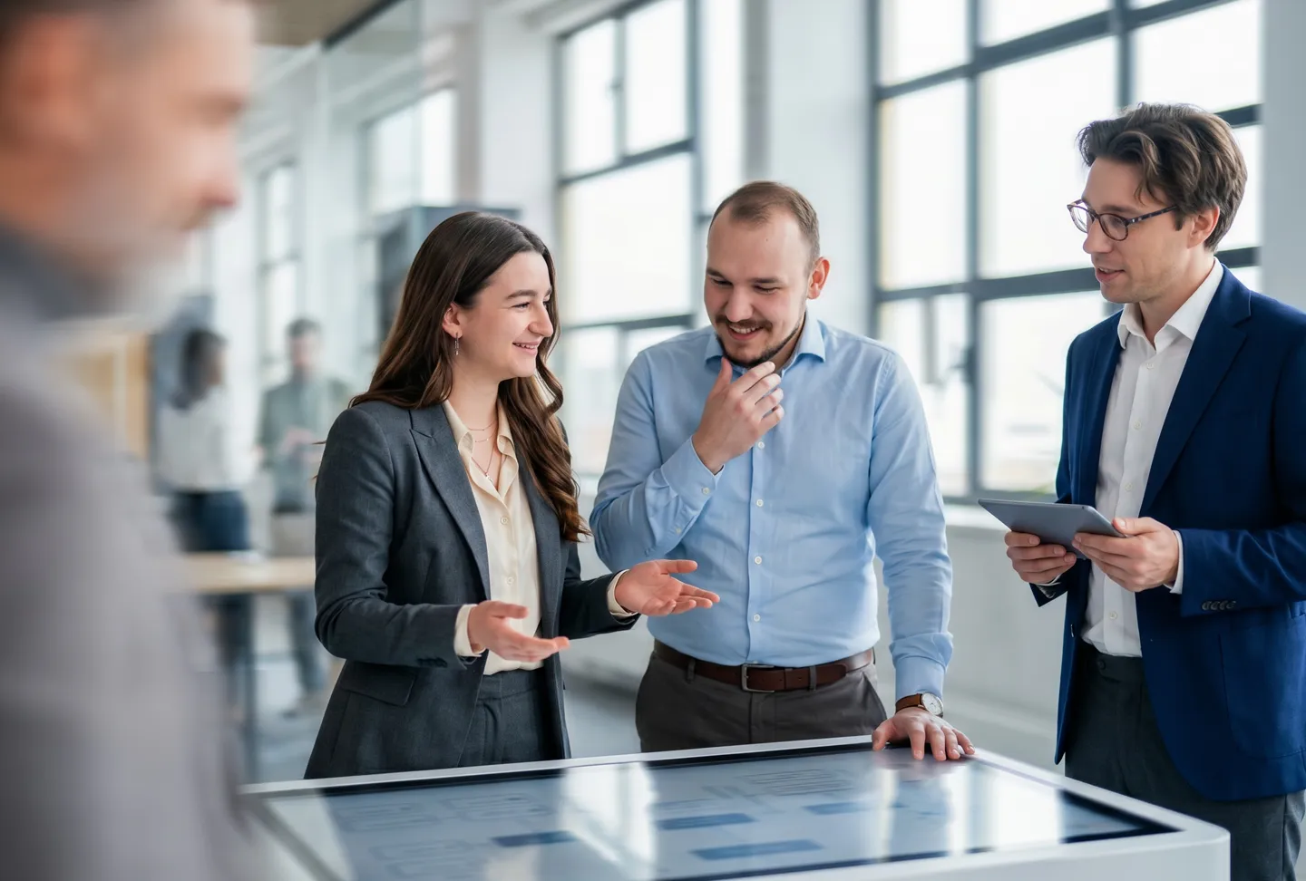 Three professionals discuss digital content on an interactive display – modern assistance and efficient teamwork in a business environment.